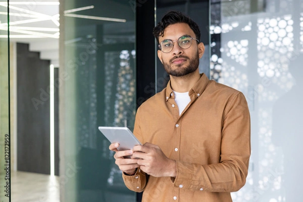 Fototapeta Confident young professional using tablet in modern office environment