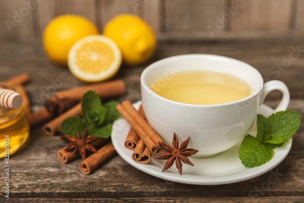 Fototapeta Fragrant hot tea with cinnamon stick and anise on a textured wooden background. A cup of hot tea with honey, lemon, mint and apples. Spicy tea with spices. Immunity tea. Health concept.Copy space.