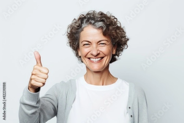 Fototapeta Portrait of a happy woman in her 50s showing a thumb up while standing against plain white digital canvas
