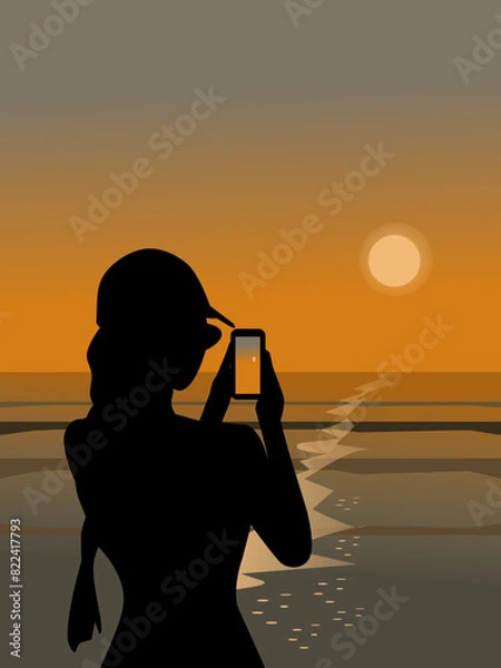 Obraz Silhouette of a woman using a mobile phone to take pictures of the sunset by the sea