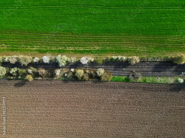 Fototapeta aerial view on an abandoned railroad track with a green and brown field surrounding