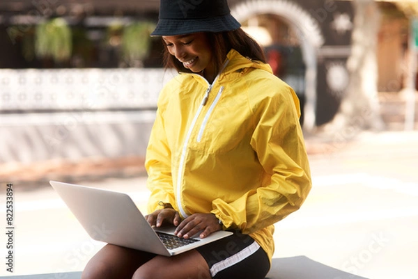Fototapeta Internet, smile and black woman with laptop in city for freelance job, connectivity or email of update. Tech, digital nomad and relax in Italy for remote work, planning or research for travel article