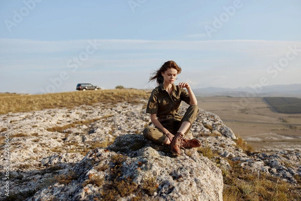 Obraz Woman sitting on rock in field with car in background, travel adventure beauty art inspired trip happiness nature enjoyment_pathway