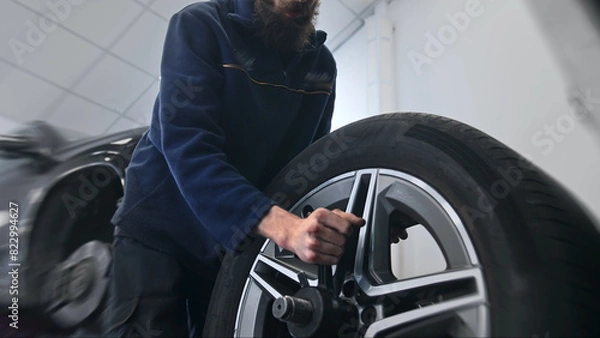Fototapeta Technician work car service. Auto mechanic balancing big wheel. 30s man change tyre cover job. Guy fix tire workshop. Worker repair vehicle. Repairman person replace cast disk. Engineer blue uniform.