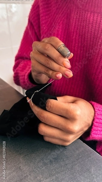 Obraz Female teen girl learning to sew by hand with needle and thimble, scrap of black fabric,pink sweater