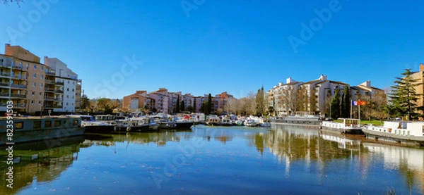 Fototapeta Peaceful Scene Along the Canal du Midi: Riverside Charm with Buildings, Riverboats on Docks, Under a Blue Sky