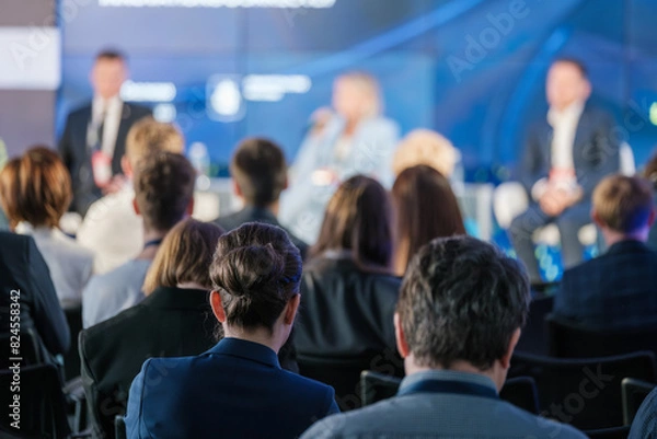 Obraz Focused audience listening to speakers at a business conference panel discussion. Event promotes networking and professional development opportunities.