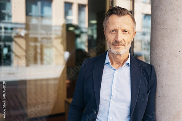 Fototapeta Portrait of a confident mature businessman standing against a pillar in an urban setting, conveying professionalism and experience.