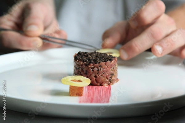 Obraz Chef's hands serving and decorating meal in restaurant kitchen