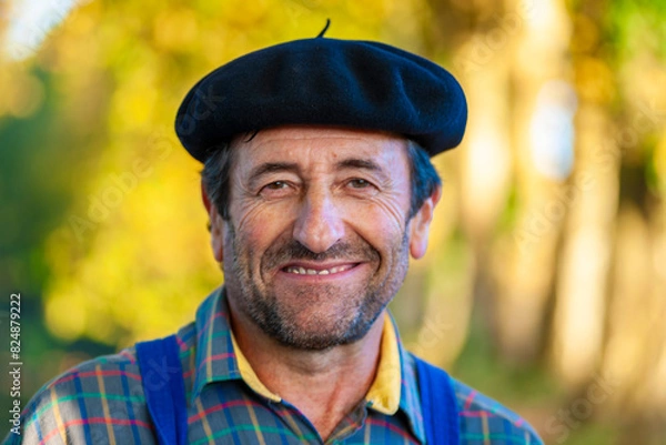 Fototapeta Portrait of a Frenchman, wearing a beret and blue dungarees smiling and gesticulating to camera