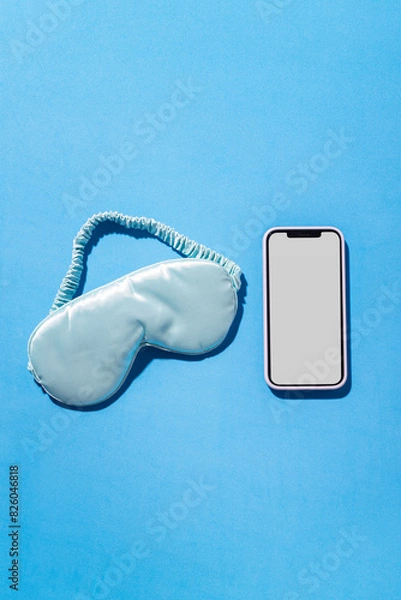 Fototapeta Vertical image of sleeping mask and smartphone with blank screen on blue empty background. Concept of healthy sleep and tracking of rhythm