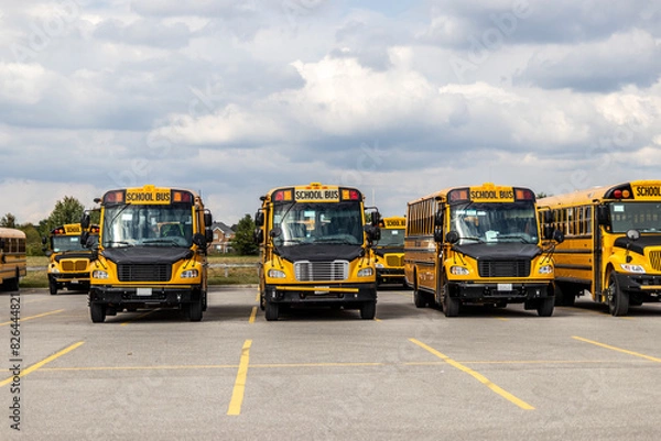 Fototapeta Yellow school buses lined up in an empty parking lot - under a partly cloudy sky. Taken in Toronto, Canada.