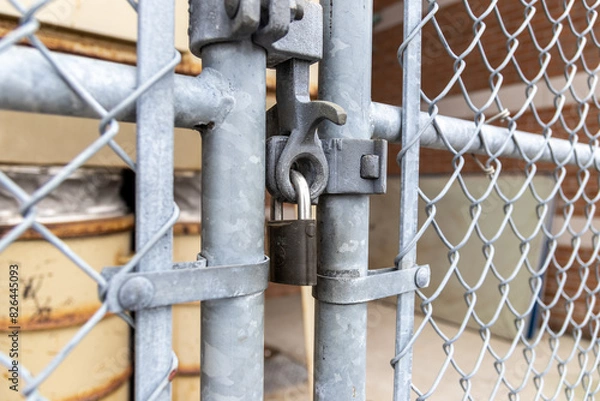 Fototapeta Close-up view of sturdy metallic padlock - chain-link fence gate - rusted metal barrels in background - industrial storage area. Taken in Toronto, Canada.