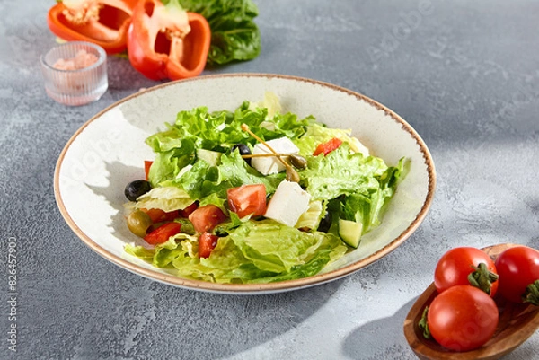 Fototapeta Greek salad with feta cheese and olives on a sunlit textured background
