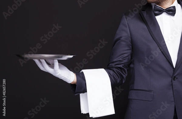 Fototapeta Waiter holding an empty silver tray against dark background