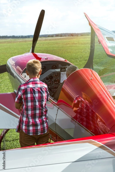 Fototapeta A Young Boy Watching And Learning How To Fly A Red Aerobatic Plane
