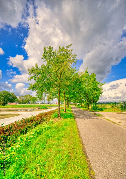 Fototapeta Big clouds almost touching the country road in a rural landscape in The Netherlands.