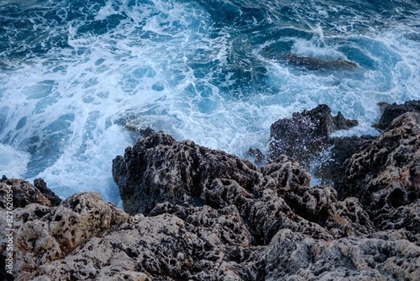 Fototapeta Beautiful view of water crashing on the rocky shore. Wave splashing against stones on shore close up.