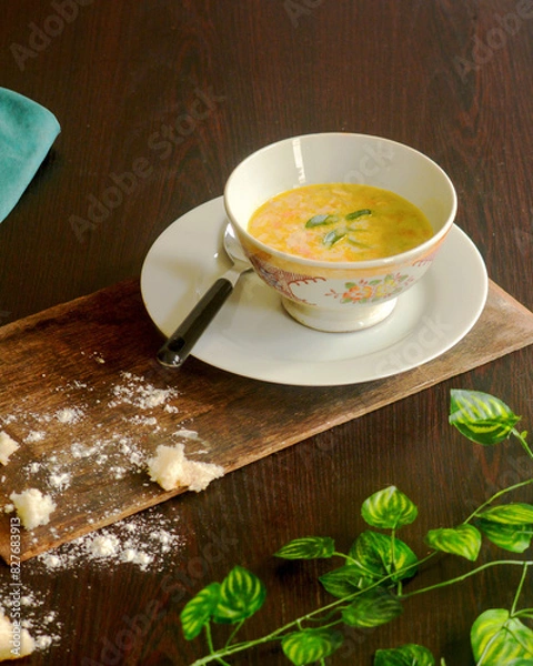 Fototapeta Creamy vegetable soup bowl on a coffee table with breadcrumbs, serviette cloth piece and green leaves