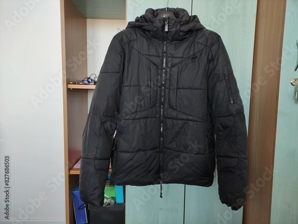 Obraz Dark winter jacket hanging on a hanger on closet door
