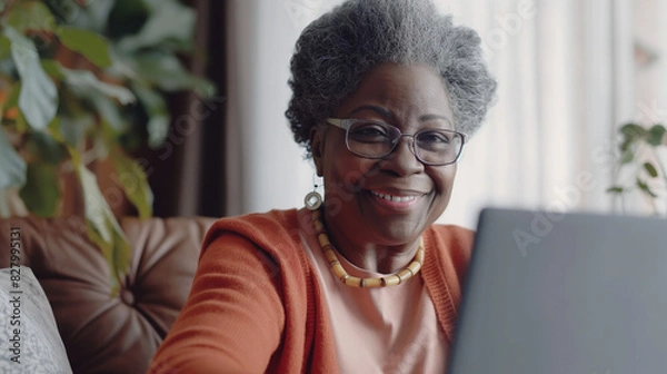 Fototapeta Elderly woman smiling while using a laptop at home
