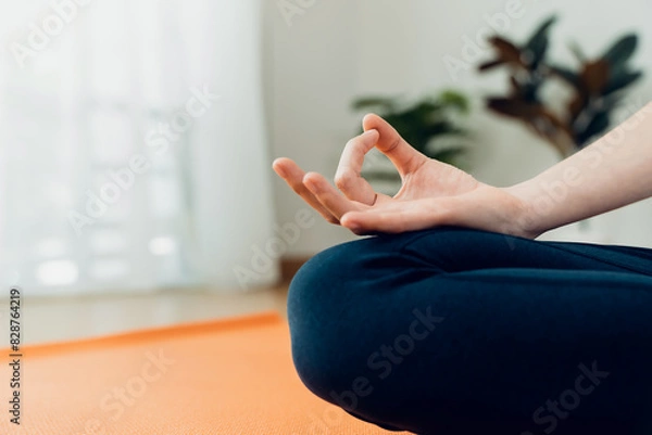 Fototapeta Woman sitting on floor in lotus pose and meditating while practicing yoga in home.