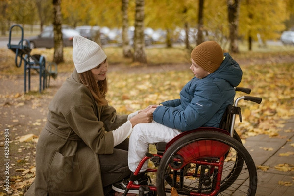 Fototapeta a 10-year-old boy in a wheelchair walks in the fall with his mother on the street with a dog on the playground. High quality photo