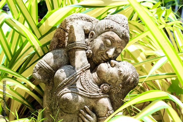 Fototapeta An ancient statue of lovers embraces serenity, surrounded by lush greenery in a tranquil setting