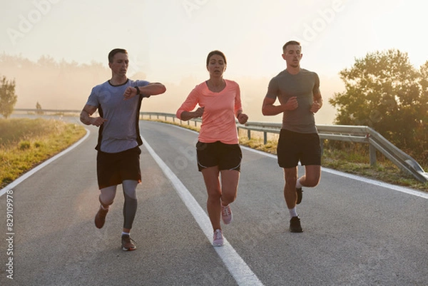 Fototapeta A group of friends, athletes, and joggers embrace the early morning hours as they run through the misty dawn, energized by the rising sun and surrounded by the tranquil beauty of nature