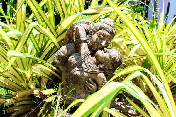 Fototapeta A stone sculpture captures the love between a couple in a vibrant garden setting with lush foliage