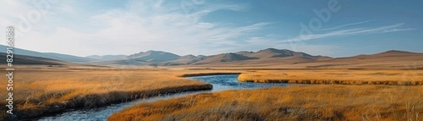 Obraz A large, open field with a river running through it. The sky is clear and the sun is shining brightly. The scene is peaceful and serene