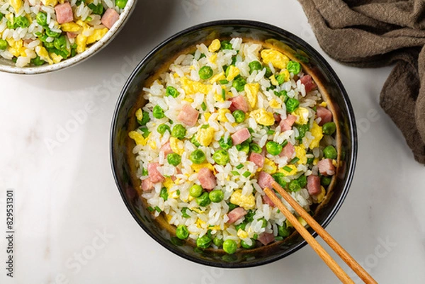 Fototapeta Cantonese Fried Rice with egg, green pea, ham steak, spring onion, ribe long rice in a dark bowl on a white table directly above.