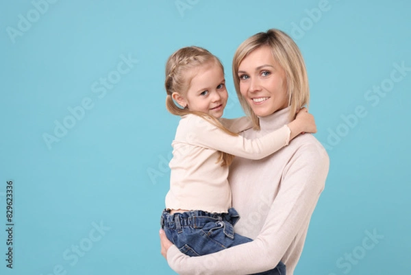 Fototapeta Daughter hugging her happy mother on light blue background. Space for text