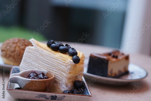 Obraz A piece of blueberry crepe cake topped with blueberry on the plate with blur of espresso macadamia cheese cake and choux cream.