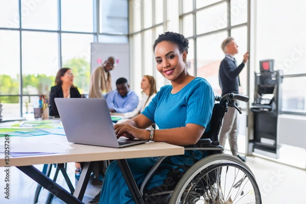 Obraz Happy, successful young disabled black female in a wheelchair, working in a tech company. in an open plan office with diverse workforce.