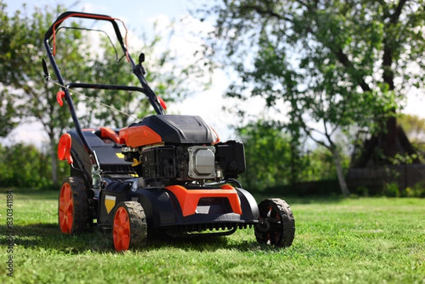 Obraz Modern lawn mower on green grass in garden