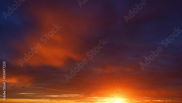 Fototapeta A breathtaking sunrise with intense orange and red tones dominating the sky, transitioning into deeper blues. The sun's rays break through the clouds, creating a warm, glowing effect. 
