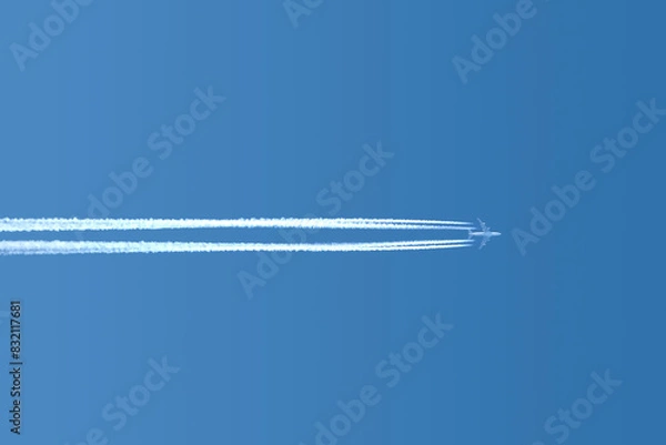 Obraz Large four engine passenger supersonic airplane flying horisontal from left to right high in blue cloudless sky leaving long white tracks