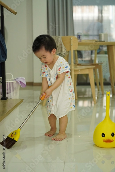 Fototapeta Asian young boy in white clothes sweeping with fantacy yellow broom set and home vibe background