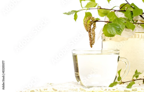 Fototapeta A transparent cup of birch sap with birch leaves