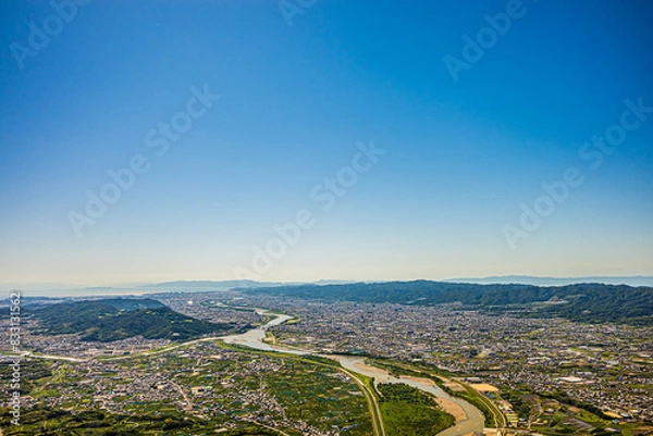 Obraz 梅雨晴れの中、紀の川上空を飛ぶパラグライダーから撮影。和歌山市街と和歌山湾