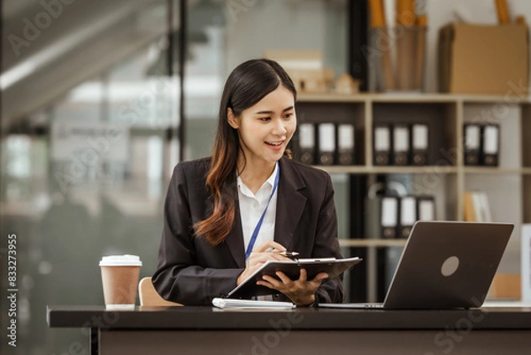 Fototapeta A young Asian businesswoman is seen diligently working at her desk. She's immersed in tasks ranging from recruitment and onboarding to performance management and diversity initiatives.