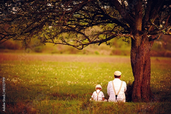 Fototapeta father and son sitting under the tree on spring lawn