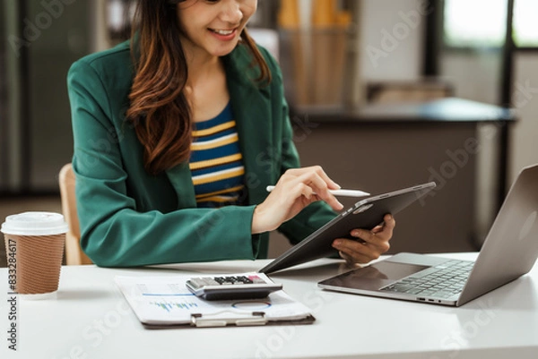 Obraz Young woman and other Asian individuals in formal suits working at desks with laptops. They engage in financial tasks including amortization, liquidity analysis, risk assessment, financial modeling.