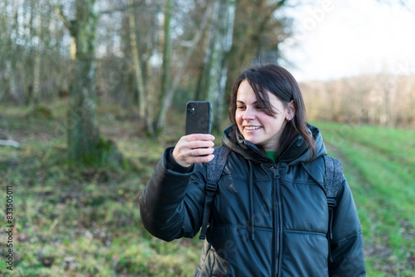 Fototapeta Young woman looking at mobile phone in the forest. Focus on smartphone.