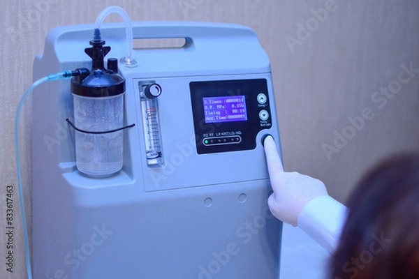 Fototapeta A hand in a medical glove turns on an oxygen generator concentrator to deliver at low lung oxygen saturation for Covid-19 pneumonia, asthma and other diseases. Rescue during the coronavirus epidemic