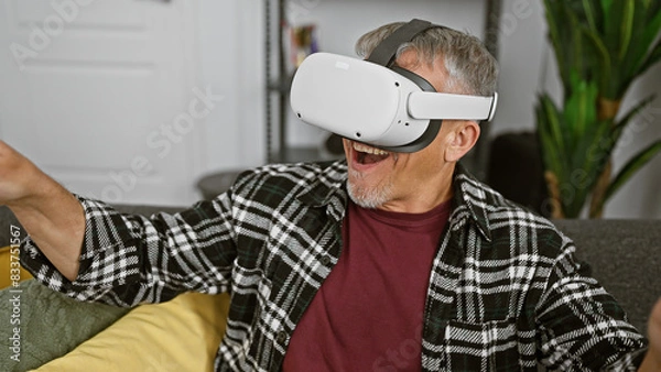 Fototapeta Excited middle-aged man with grey hair using virtual reality headset in a modern living room.