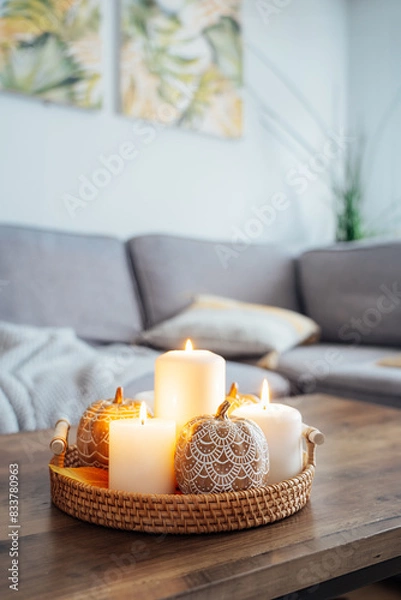 Fototapeta Autumn fall cozy mood composition for hygge home decor. Orange pumpkins decorated with mandalas, burning candles on wicker tray on the coffee table in the living room. Selective focus. Copy space.