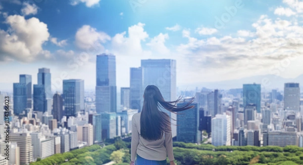 Fototapeta 日本の街・都市・朝日を受けたオフィスビル群を前に佇み風を受けて髪をなびかせる会社員の女性の出勤　ビジネス・はじまり・決意・目標・挑戦のイメージ