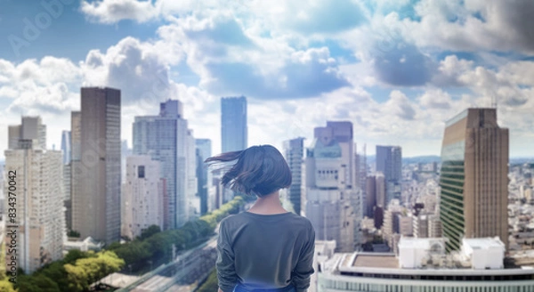 Fototapeta 日本の街・都市・朝日を受けたオフィスビル群を前に佇み風を受けて髪をなびかせる会社員の女性の出勤　就職・ビジネス・はじまり・決意・目標・挑戦のイメージ